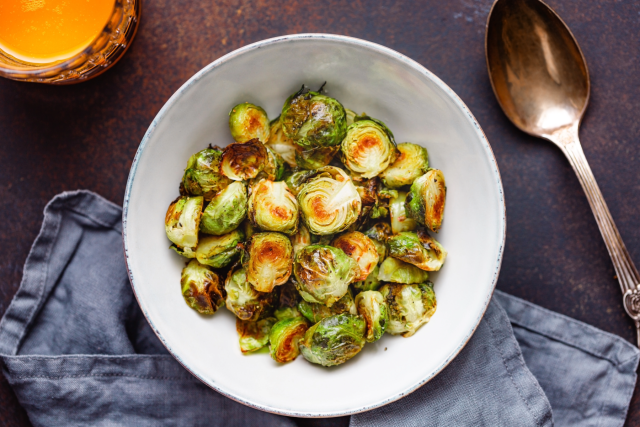 Roasted Brussels sprouts in white bowl with spoon and cloth napkin.