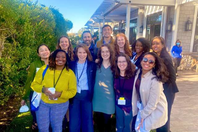group of 12 people next to a hedge and building posing for a picture