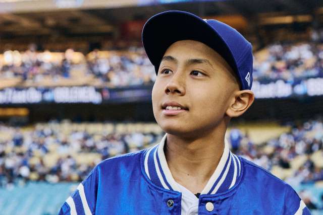 A teen oncology patient is on the field at Dodger Stadium dressed in Dodgers gear.