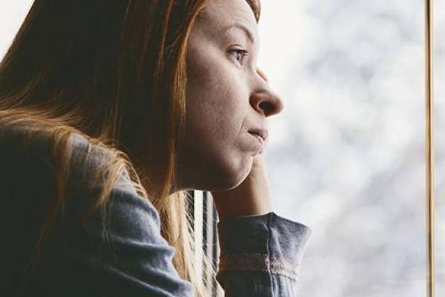 Young woman looking sadly out window
