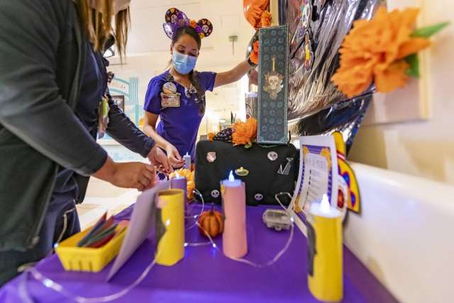 Close-up of a decorated table with colorful candles, marigold flowers, and craft supplies for a Day of the Dead display.
