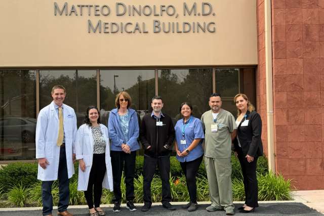 Patient smiling with group of medical team in front of building