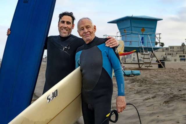 Dr. Sassoon and Robert Lombard standing with their surfboards in front of Lifeguard tower 4