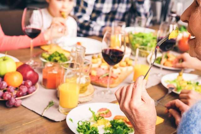 People enjoying a meal together with salads, fresh fruit, orange juice, and glasses of red wine on a wooden table.