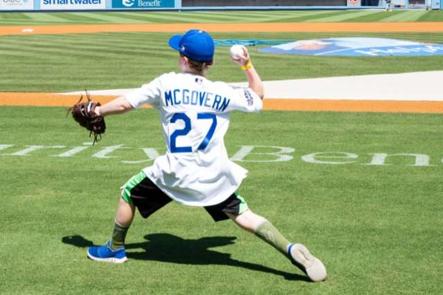 Kellen McGovern in a baseball jersey throws a ball on a grassy field.
