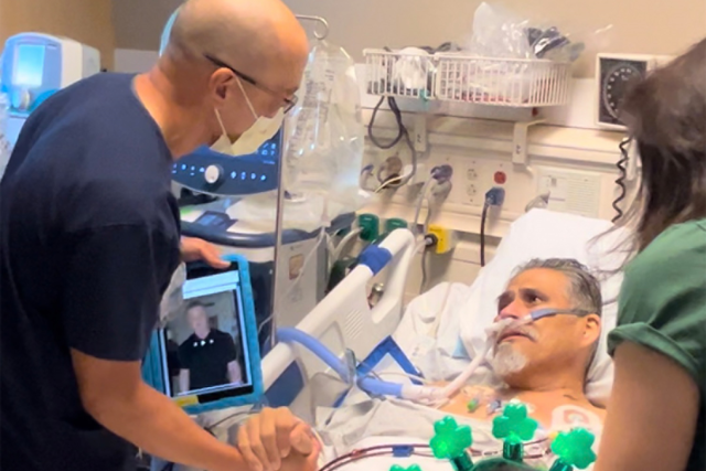 Paul Aguilar is in his hospital bed, with nurse David Yamada standing by his side, grasping his hand. Yamada is also holding a tablet with the message from Sylvester Stallone.