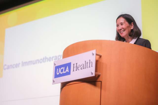A doctor is on stage, addressing an audience from behind a podium.
