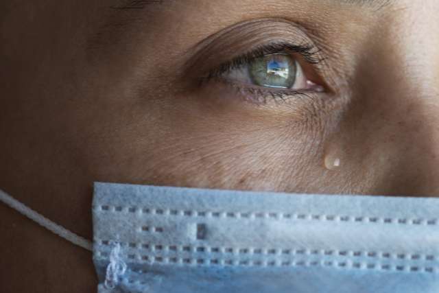 Close-up of a woman’s eye with a tear, wearing a blue face mask.