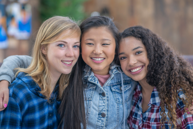 Three ladies standing shoulder to shoulder with arms around each other