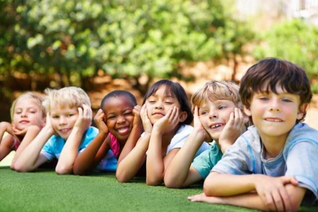A group of children lying together in the grass, smiling