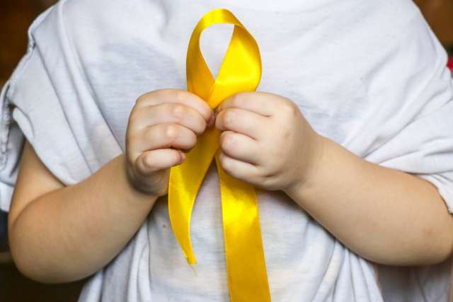 Child holding gold cancer ribbon in support of childhood cancer