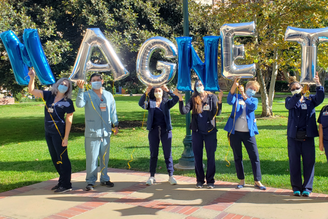 a group of healthcare workers standing outside holding blue and silver balloon letters that spell out "MAGNET"