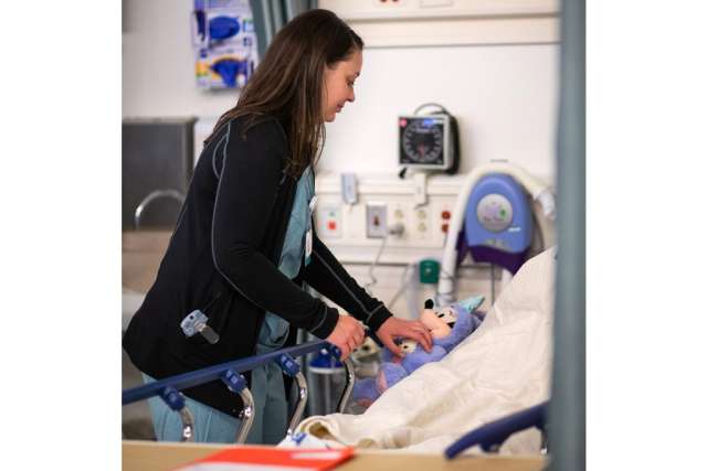 Karleen Wray handing a Minnie Mouse stuffed animal to a child patient who is recovering from her surgery