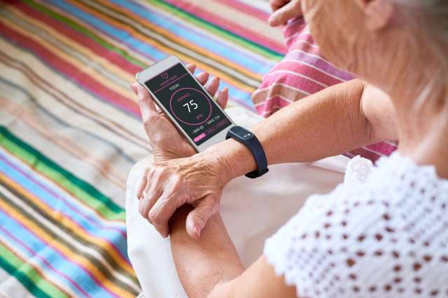Person wearing a smartwatch checking a heart-rate app on a smartphone