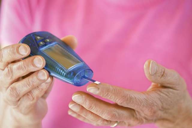 A woman's hands utilizing a glucose blood glucose monitor on herself, by holding it up to her finger.