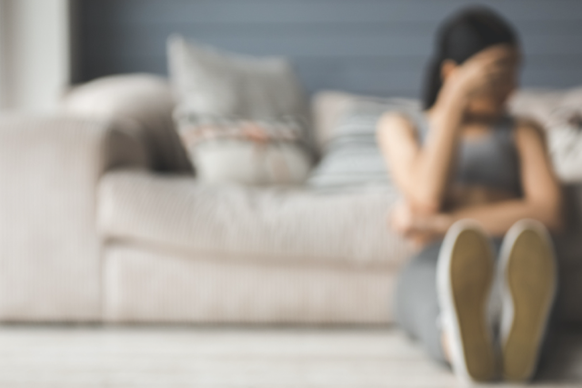 Teenage girl sitting on the floor, with her back on the couch.