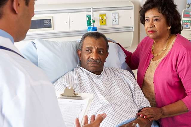 Patient in a hospital bed with a healthcare professional holding a clipboard and another person standing beside.