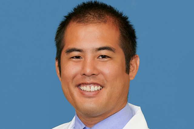 Jeffrey Fujimoto smiling in white lab coat and tie on blue background