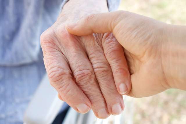 A young person holding an older person in a wheelchair by the hand