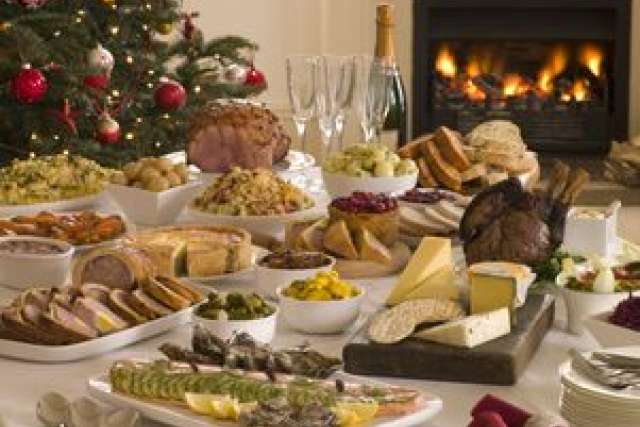 A festive holiday table filled with various dishes, cheese, and a warm fireplace in the background.