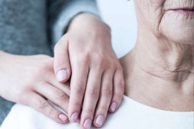 Caregiver's hands resting on an elderly woman's shoulder