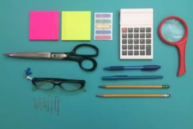 Office supplies arranged on a teal background: scissors, calculator, glasses, and sticky notes.