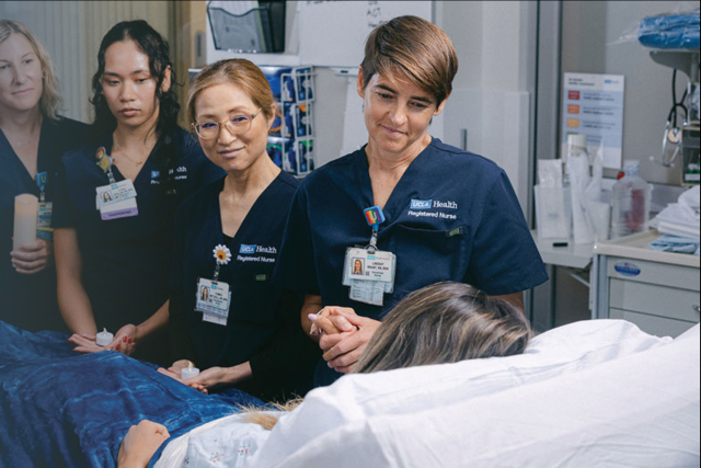 A group of healthcare professionals stands by a patient in a hospital setting.