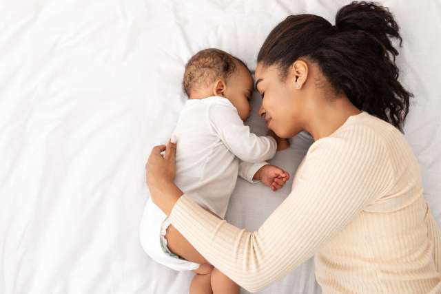 Mother Hugging Sleeping Baby Lying In Bed Indoor