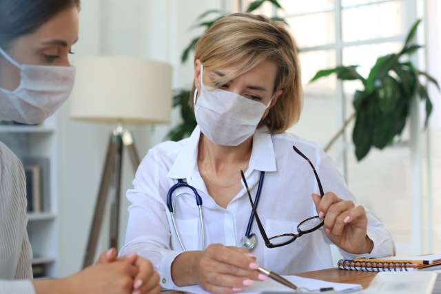 Doctor therapist in medical mask on consultation with patient in office.