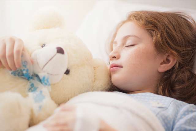 Adorable little girl resting in a hospital bed with her teddy bear.