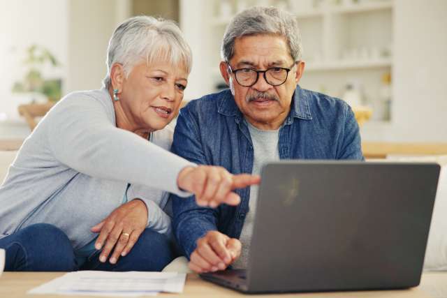 Older couple on couch pointing at a laptop screen