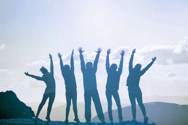 Group of people standing on mountain top with hands up in the air