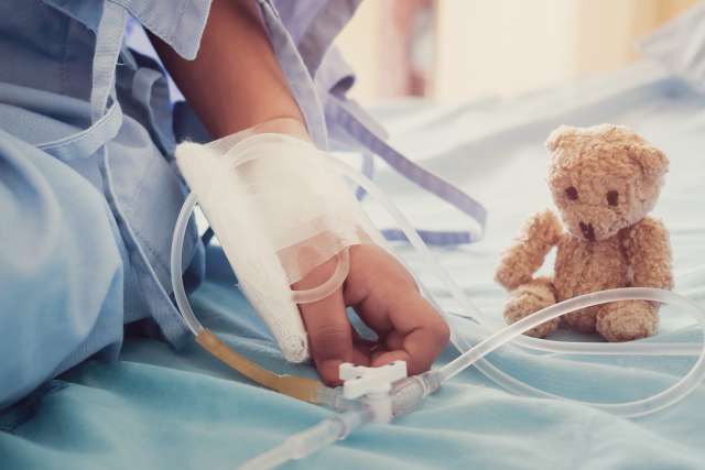 Child's hand and small teddy bear on hospital bed