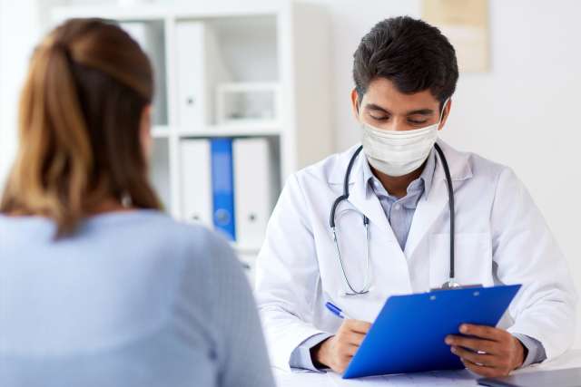 Doctor wearing protective medical mask with clipboard and patient at hospital