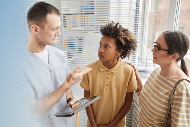 Male nurse holding a tablet talking to an adolescent and his mother.