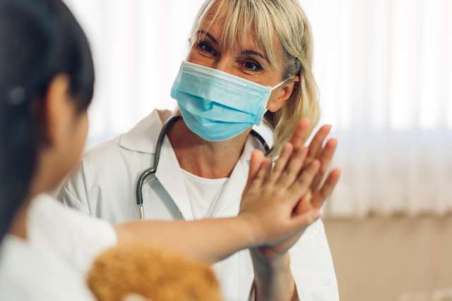 Woman doctor wearing protective mask talking to little girl patient