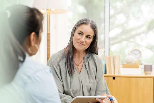 Two women engaged in a conversation, one holding a tablet, in a bright, modern space.