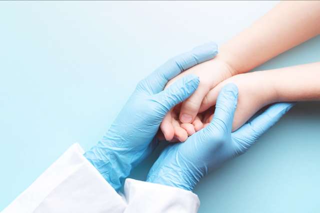 Doctor's hands in gloves holding child's hands.