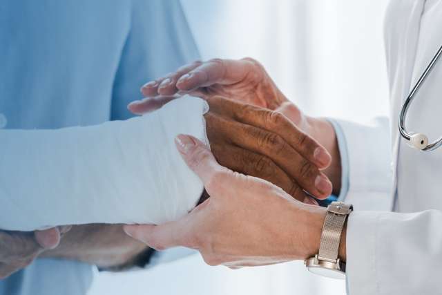 Doctor touching broken arm of man in clinic