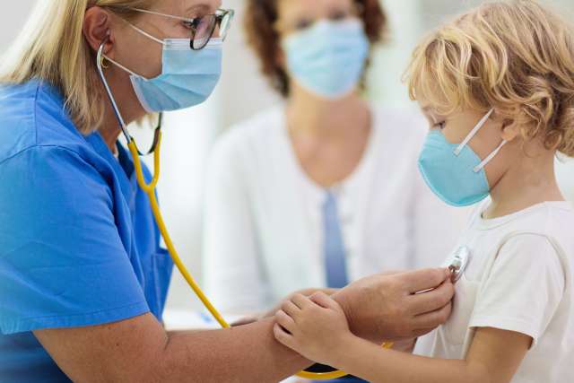 Doctor examining sick child in face mask
