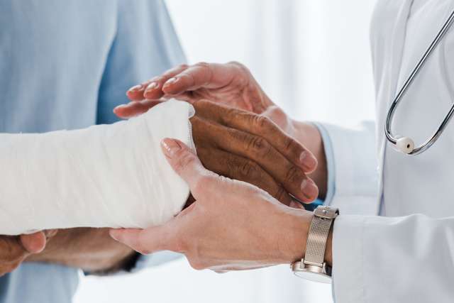 Doctor wearing white coat holding a patient's hand that has been wrapped in a bandage