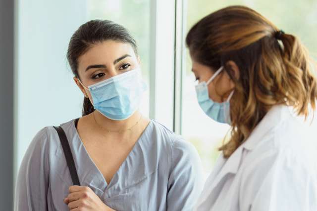 Female patient and doctor discussing while wearing masks