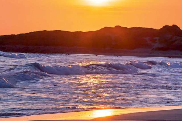 Sunset with mountains and ocean waves.