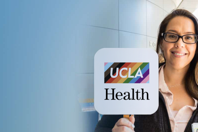 A woman holding a UCLA Health sign, with UCLA in a rectangle of the pride rainbow