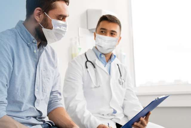 Doctor with clipboard and patient wearing masks meeting at hospital 