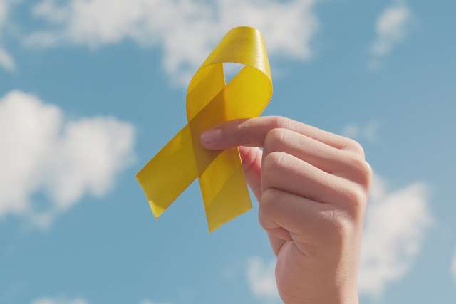 Hands holding yellow gold ribbon over blue sky
