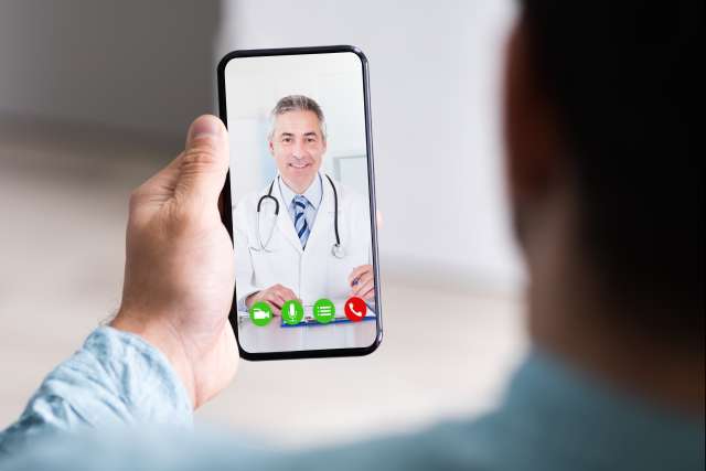 Close-up, over-the-shoulder view of a person holding a smartphone, video calling a doctor (telemedicine/telehealth).