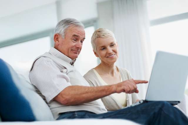 Two people sitting on a couch looking at a laptop, one pointing at the screen.