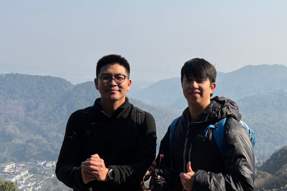 Two hikers with trekking poles standing on a ridge overlooking a mountain valley.