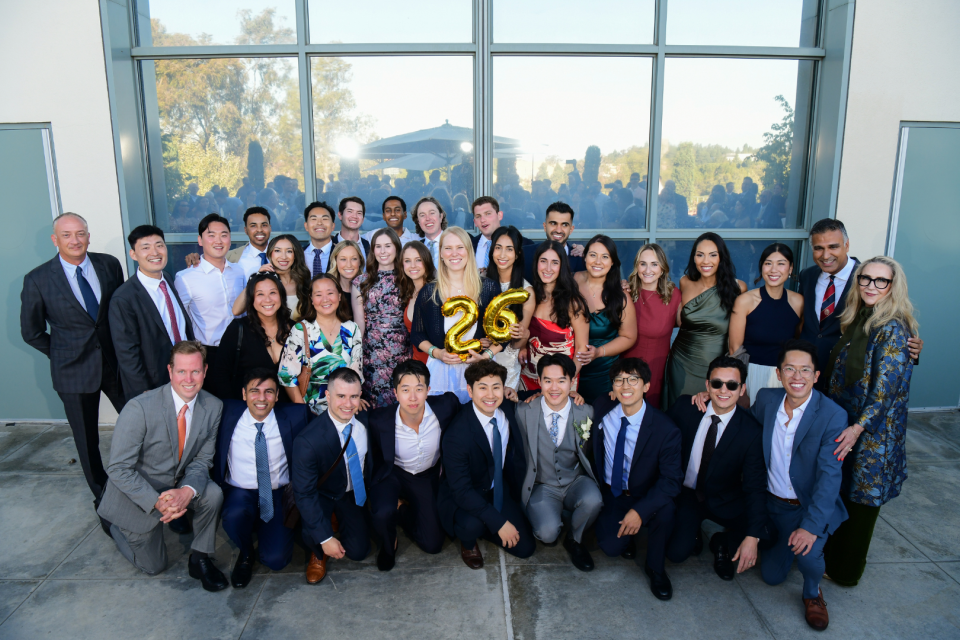 Large group of professionally dressed people posing outdoors by tall windows
